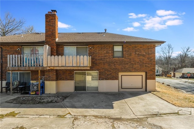 rear view of property featuring a balcony, a garage, brick siding, concrete driveway, and a chimney