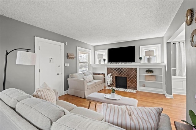 living area with a fireplace, wood finished floors, baseboards, and a textured ceiling