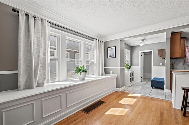 hall featuring visible vents, a textured ceiling, light wood-style floors, crown molding, and a decorative wall