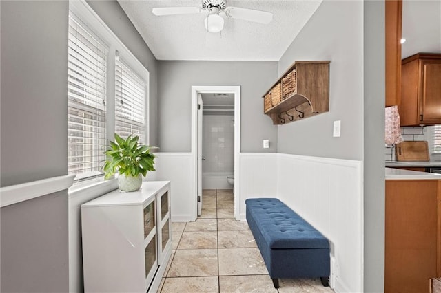 clothes washing area with light tile patterned floors, a wainscoted wall, a textured ceiling, and ceiling fan