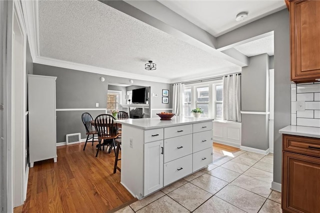 kitchen with visible vents, brown cabinets, a textured ceiling, light countertops, and decorative backsplash