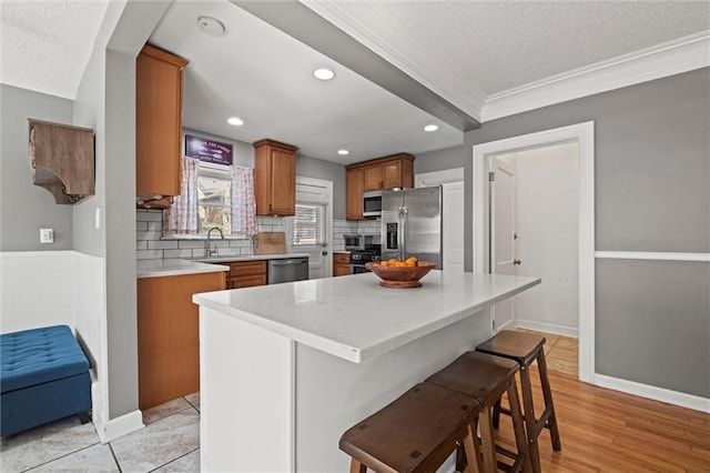 kitchen featuring light countertops, decorative backsplash, brown cabinetry, stainless steel appliances, and a sink