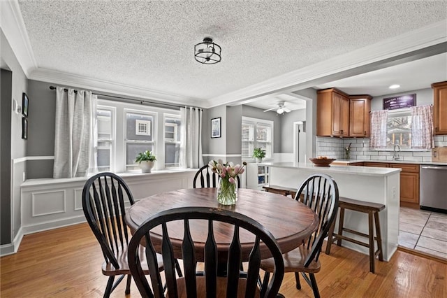 dining room with light wood-type flooring, a ceiling fan, a wainscoted wall, and crown molding