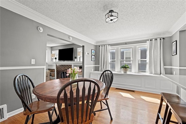 dining area with visible vents, light wood-style flooring, a fireplace, and crown molding