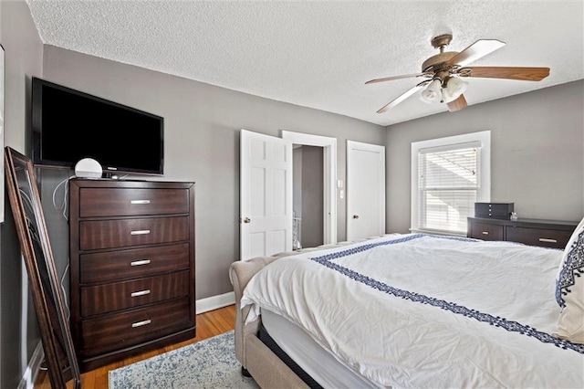 bedroom with ceiling fan, baseboards, a textured ceiling, and wood finished floors