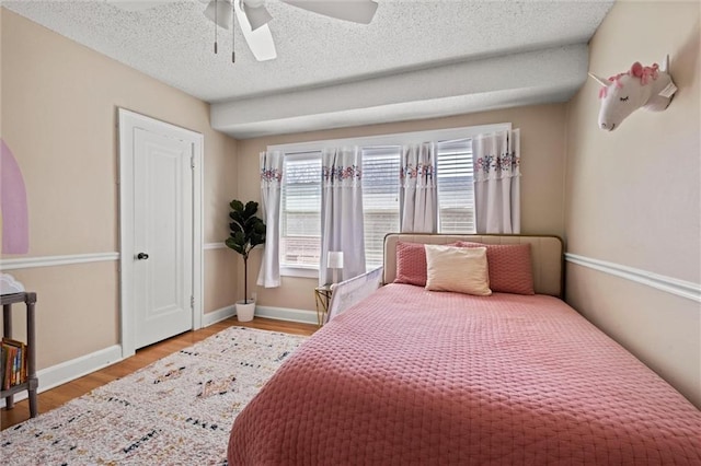 bedroom featuring ceiling fan, a textured ceiling, baseboards, and wood finished floors