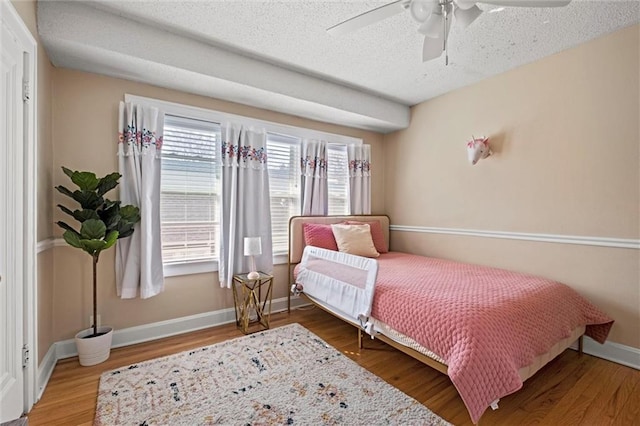 bedroom with ceiling fan, a textured ceiling, baseboards, and wood finished floors