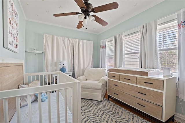 bedroom with a crib, ceiling fan, dark wood-style flooring, and ornamental molding