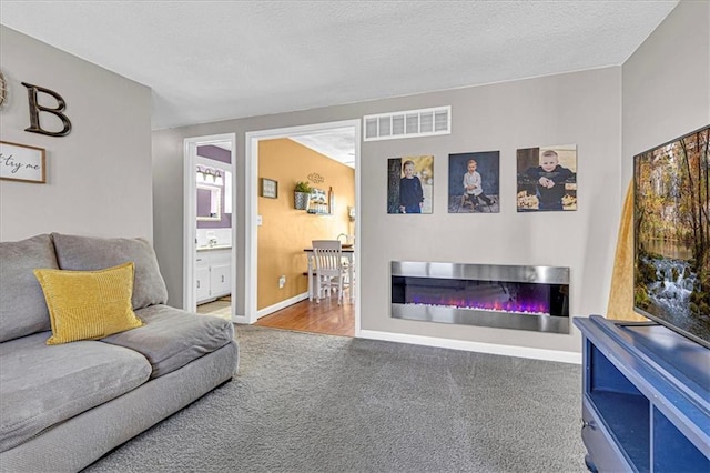 living area featuring carpet floors, visible vents, a glass covered fireplace, a textured ceiling, and baseboards