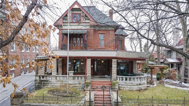 victorian home featuring covered porch, stone siding, brick siding, and a fenced front yard