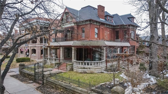 rear view of property with brick siding, a fenced front yard, a chimney, and a balcony