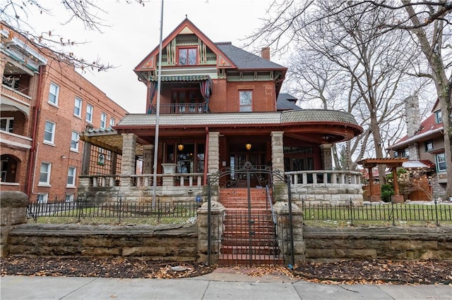 victorian house with a porch, stairway, a chimney, and a fenced front yard