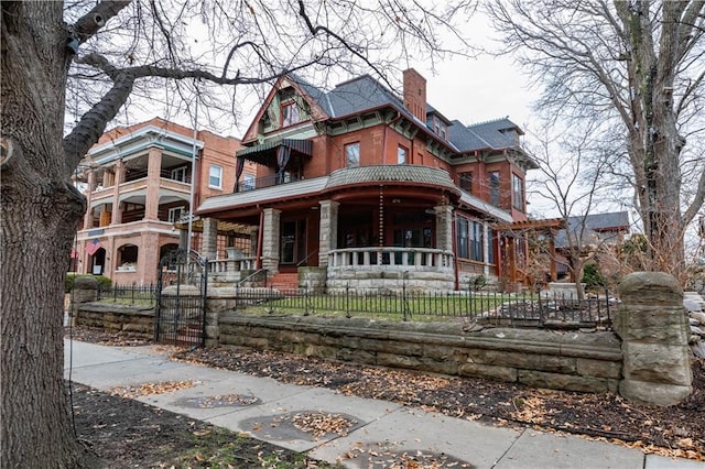 victorian home featuring covered porch, a fenced front yard, and a chimney