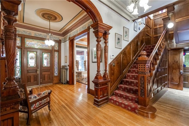 entrance foyer featuring ornamental molding, light wood-type flooring, arched walkways, and stairway