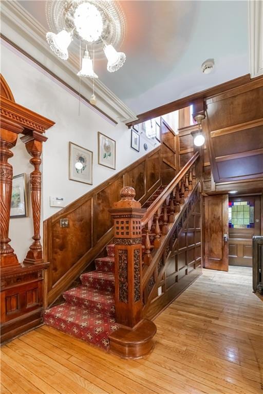 stairway with a wainscoted wall, crown molding, a notable chandelier, and hardwood / wood-style flooring