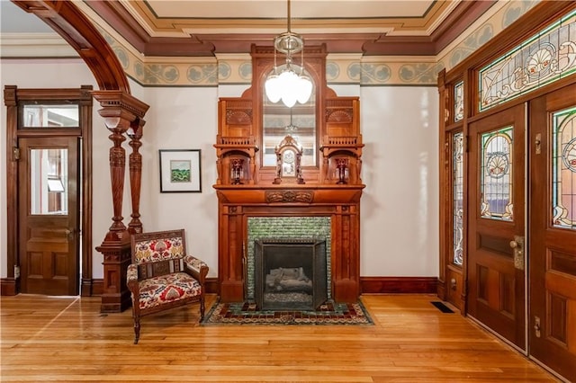 interior space with visible vents, a tiled fireplace, ornamental molding, and wood finished floors