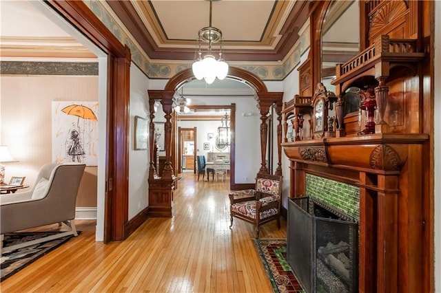 hallway with arched walkways, crown molding, ornate columns, light wood-type flooring, and baseboards