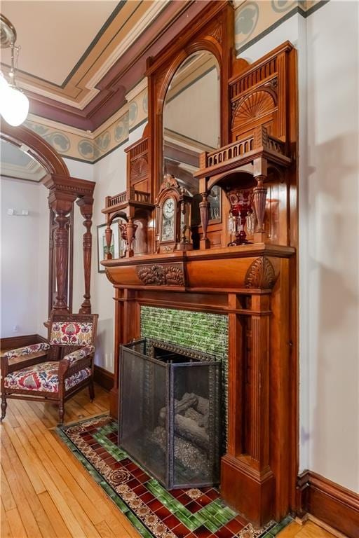 living area with arched walkways, a fireplace, crown molding, hardwood / wood-style floors, and baseboards