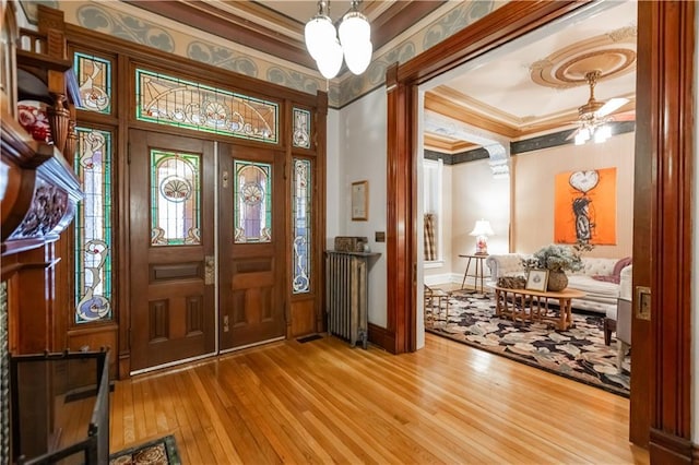 entrance foyer featuring ornamental molding, wood-type flooring, a chandelier, and radiator heating unit