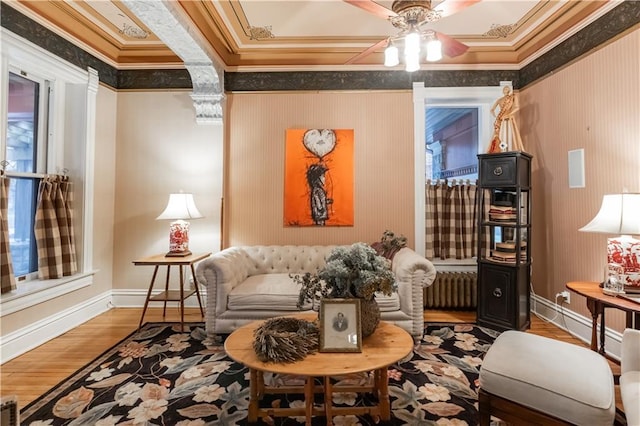 living area with wood finished floors, a ceiling fan, baseboards, radiator, and crown molding