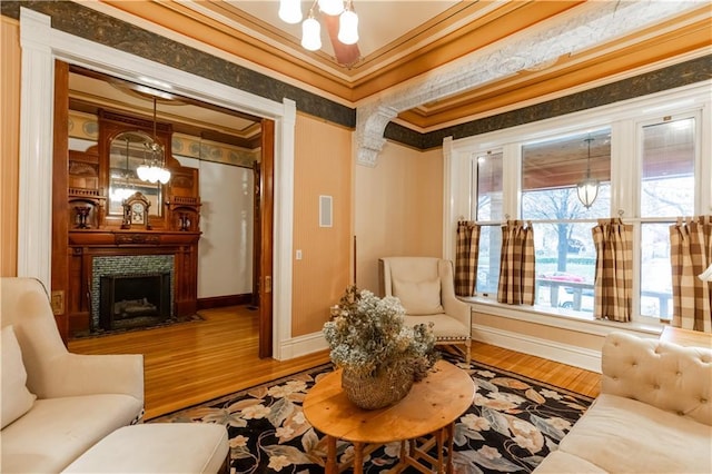 living area with ornamental molding, a fireplace, baseboards, and wood finished floors