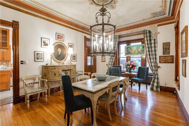 dining space featuring crown molding, a notable chandelier, light wood-style flooring, and baseboards