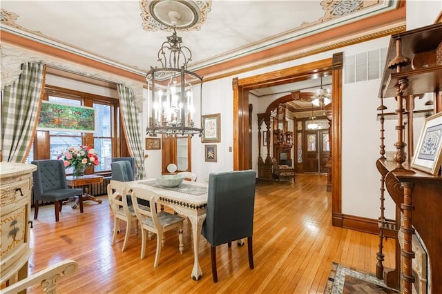 dining area featuring a chandelier, arched walkways, crown molding, and light wood-style flooring