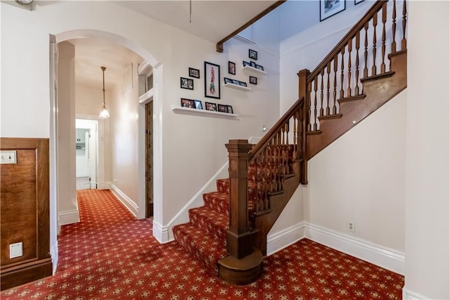 stairway with arched walkways, carpet flooring, and baseboards