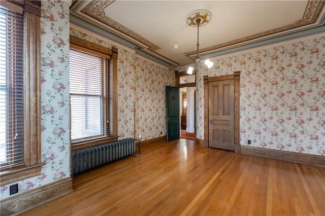 unfurnished dining area with radiator, ornamental molding, light wood-type flooring, baseboards, and wallpapered walls