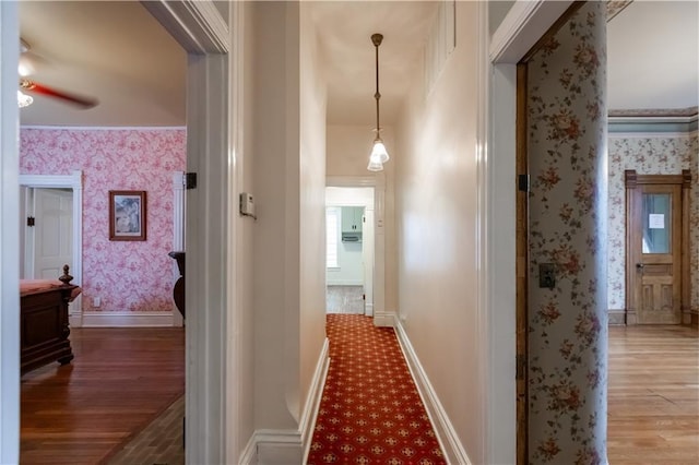 hall featuring wallpapered walls, light wood-style flooring, baseboards, and ornamental molding