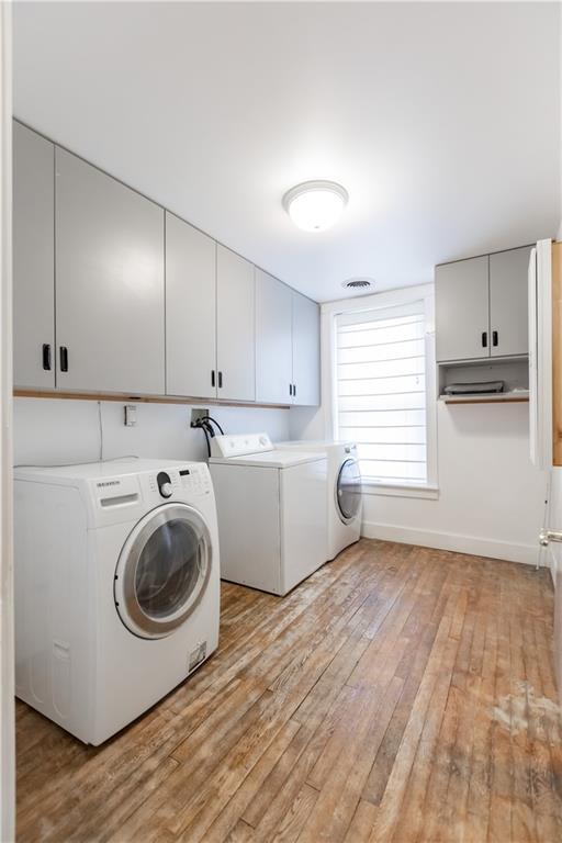 washroom featuring light wood finished floors, cabinet space, visible vents, washer and dryer, and baseboards