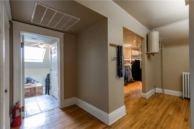 hallway featuring radiator, light wood-style flooring, visible vents, and baseboards