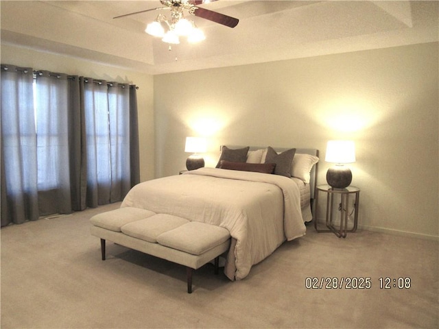 bedroom with a raised ceiling, light carpet, ceiling fan, and baseboards