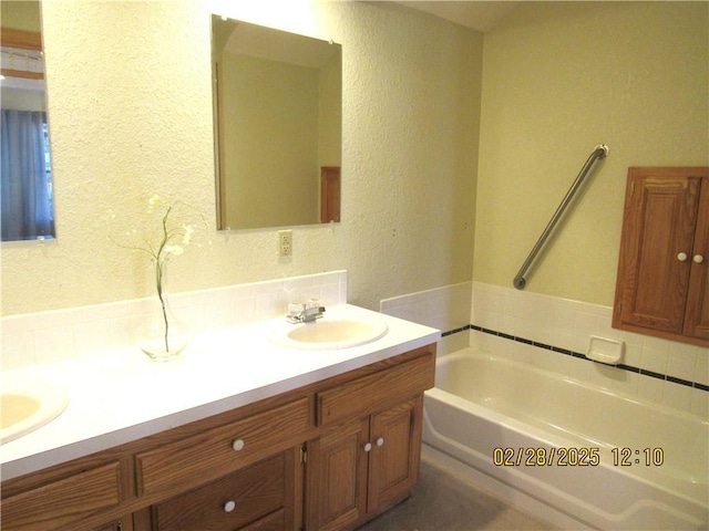 full bath featuring a textured wall, double vanity, a sink, and a bath