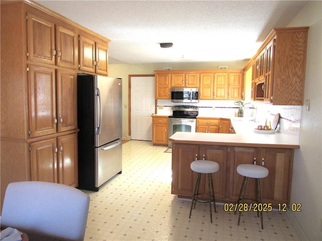 kitchen with stainless steel appliances, a peninsula, light countertops, light floors, and a kitchen bar