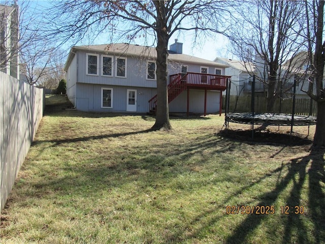 rear view of property with a trampoline, a yard, stairway, a deck, and a fenced backyard