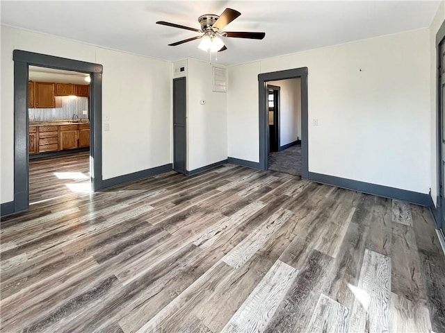 empty room with a ceiling fan, a sink, baseboards, and wood finished floors