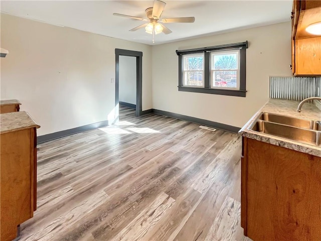 unfurnished dining area with ceiling fan, light wood-type flooring, a sink, and baseboards