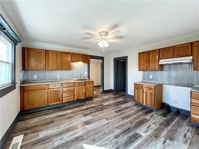 kitchen with under cabinet range hood, brown cabinetry, a sink, and light countertops