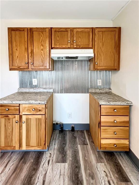 kitchen with baseboards, dark wood-style flooring, brown cabinetry, and under cabinet range hood