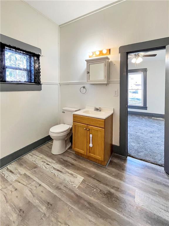 bathroom featuring ceiling fan, toilet, wood finished floors, vanity, and baseboards