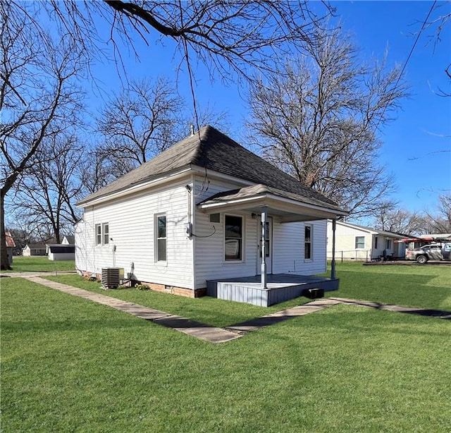 exterior space with covered porch, a shingled roof, central AC, and a yard