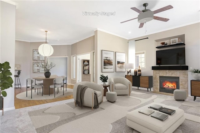 living room featuring baseboards, a tiled fireplace, ceiling fan, ornamental molding, and wood finished floors