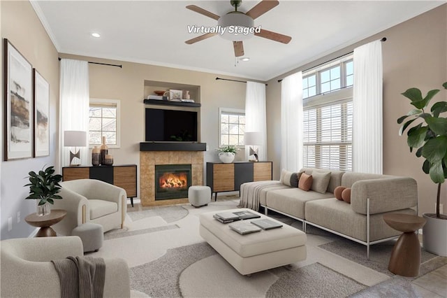 living room featuring ceiling fan, a tiled fireplace, crown molding, and recessed lighting