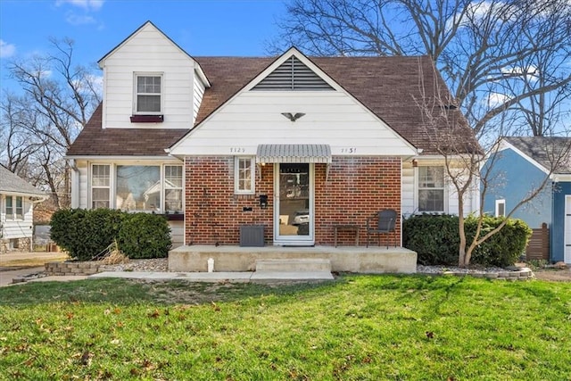 view of front facade featuring cooling unit, a front yard, roof with shingles, and brick siding
