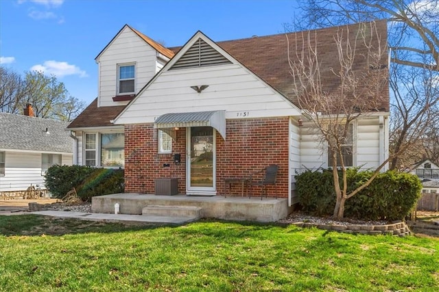 view of front of home with a shingled roof, brick siding, and a front lawn