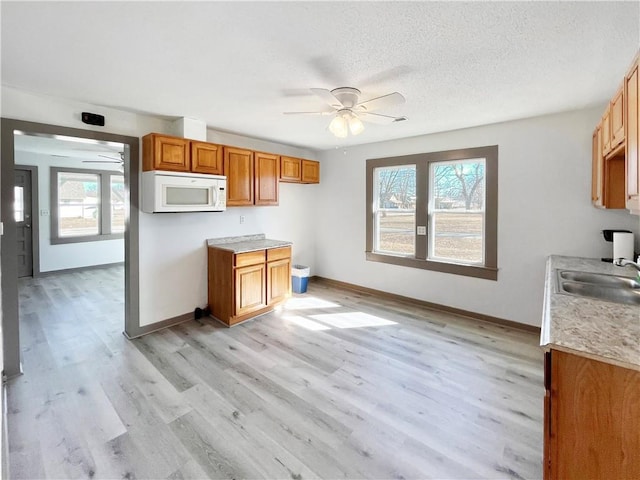 kitchen with white microwave, ceiling fan, light countertops, light wood-type flooring, and a sink