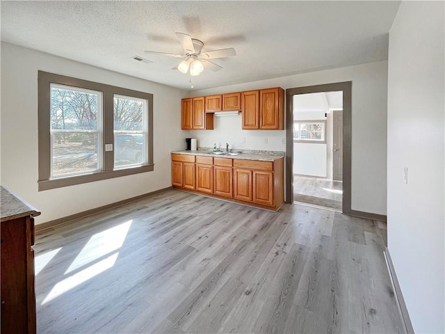 kitchen featuring visible vents, baseboards, light wood-style floors, light countertops, and brown cabinetry