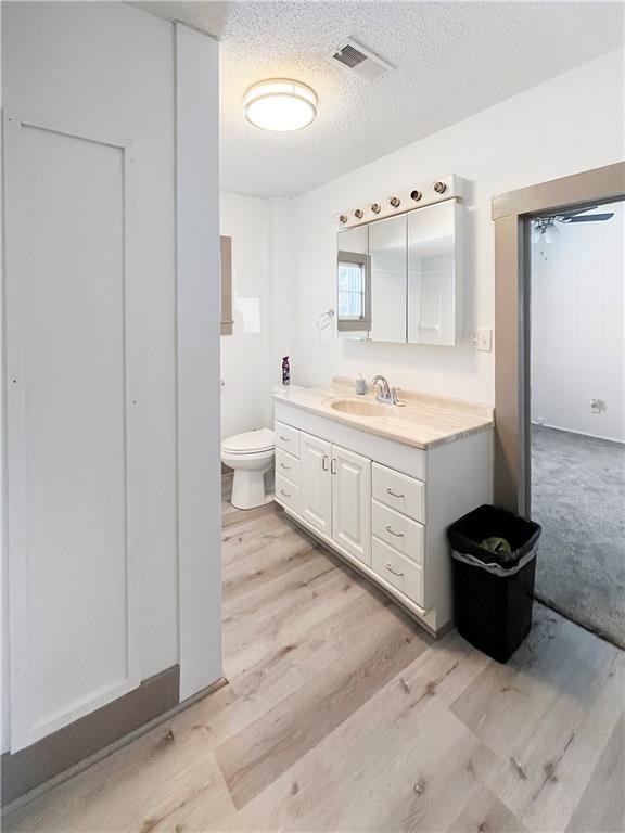 bathroom featuring a textured ceiling, toilet, wood finished floors, vanity, and visible vents