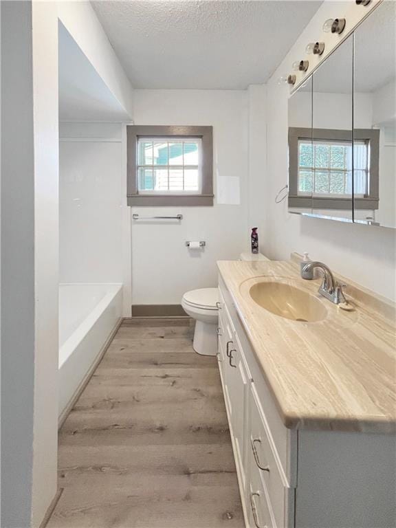 bathroom featuring a textured ceiling, plenty of natural light, wood finished floors, and toilet